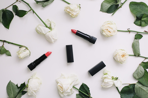Composition with white roses and red lipsticks. Flat lay on white table, top view.