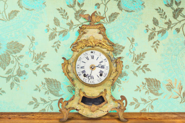 istock Authentic eighteenth century weathered table clock in front of wallpaper with flower pattern 1309754926