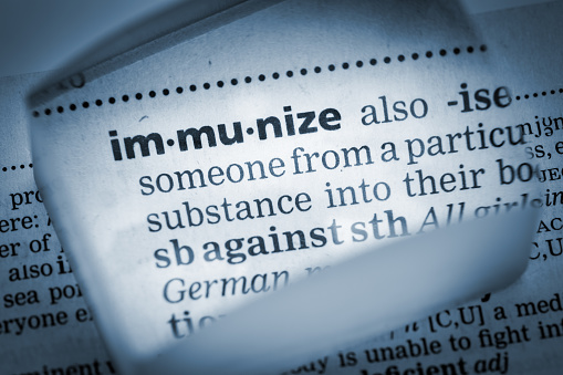 The Dictionary definition of the word “Immunize” photo taken through magnifying glass from a page of a dictionary with selective focus.