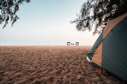Tent under pine trees, chairs and camping table on the sand in front of the tent, camping at the beach on vacation.