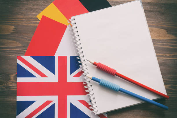 istock Three national flags, German, English, French, and notebook with blank sheets and two pencils on brown wooden surface. The concept of foreign language courses 1309760652