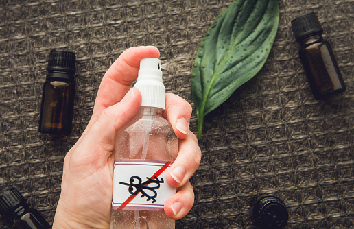 Woman hand holding and using homemade essential oil based mosquito repellent. Flat lay view of spray bottle surrounded by brown essential oil bottles against black background.