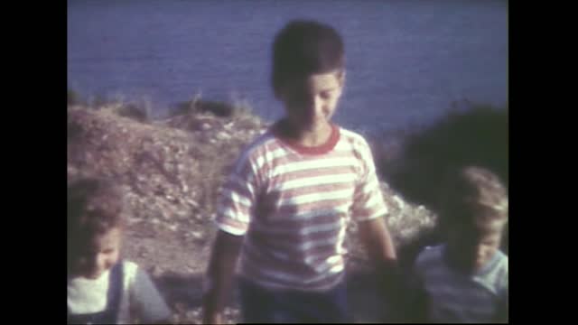 Children try to climb a small wall and walk in front of the sea in 1959 8mm FDV
