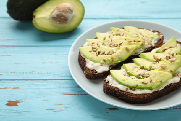 istock Avocado sandwich on dark rye bread made with fresh sliced avocados on blue background. 1309764564