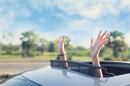 mujer sacando las manos de la parte superior del techo corredizo del coche, conduciendo por una carretera rural photo