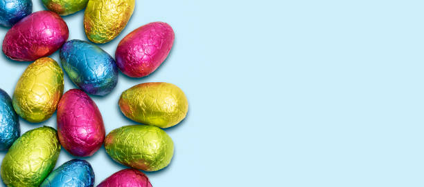 istock Side border of colorful wrapped chocolate Easter eggs on blue background. Top view. 1309770764