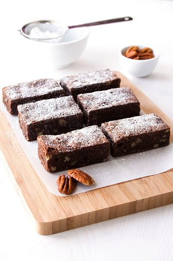 Freshly baked homemade chocolate brownies cooling on a wooden chopping board. 
Sprinkled with icing sugar.