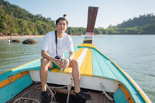Young man sitting on head of long tail boat and sightseeing happy with beautiful scenics sea view in Krabi, Thailand