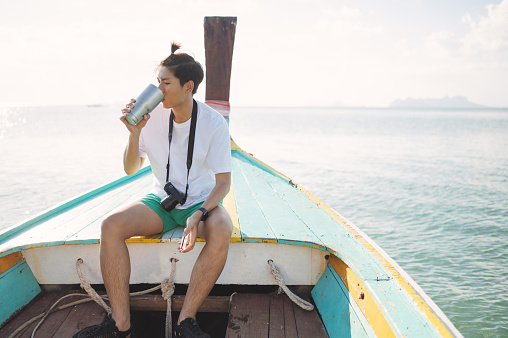Traveling in Thailand. Asian toursit man sitting on the head of wooden longtail boat travel on the sea go to the amazing island and lagoon nature in vacation.Phi Phi Island