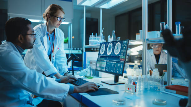 istock Female Research Scientist Has a Conversation with Bioengineer About the Effects of Different Pharmaceutical Drugs on Brain. They Look at Computer Software Visualization in a Modern Science Laboratory. 1309776193