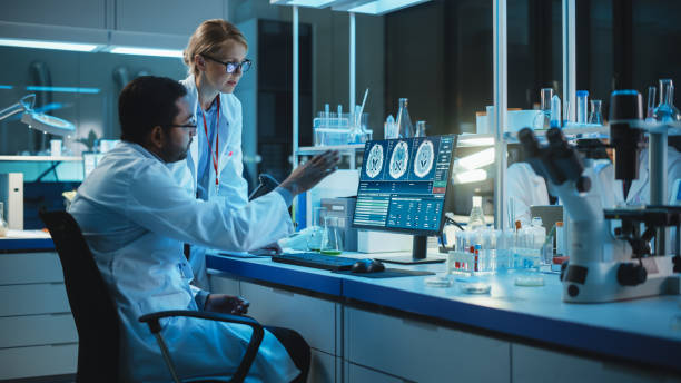 istock Female Research Scientist Has a Conversation with Bioengineer About the Effects of Different Pharmaceutical Drugs on Brain. They Look at Computer Software Visualization in a Modern Science Laboratory. 1309776209
