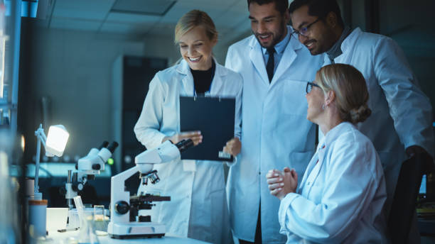 istock Happy Female Reseach Scientist Makes an Important Discovery While Researching Samples Under the Microscope. Happy Colleagues Celebrate it and Share Success with Fellow Bioengineers. 1309776211