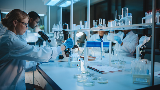 A female scientist examines samples in a laboratory, full of, state of the art research equipment. The NMR apparatus is discovering diseases such as autism, diabetes, dementia and cancer. This biochemist is holding and looking at samples.
