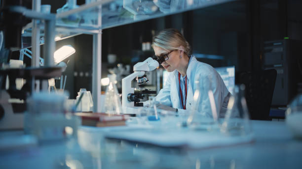 istock Medical Development Laboratory: Caucasian Female Scientist Looking Under Microscope, Analyzes Petri Dish Sample. Specialists Working on Medicine, Biotechnology Research in Advanced Pharma Lab 1309776230