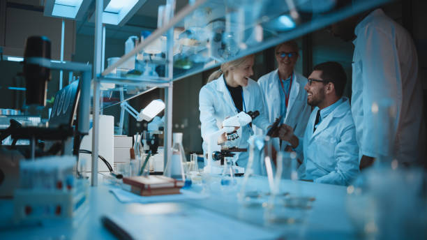 istock Happy Male Reseach Scientist Makes an Important Discovery While Researching Samples Under the Microscope. Happy Colleagues Congratulate it and Share Success with Fellow Bioengineers. 1309776235