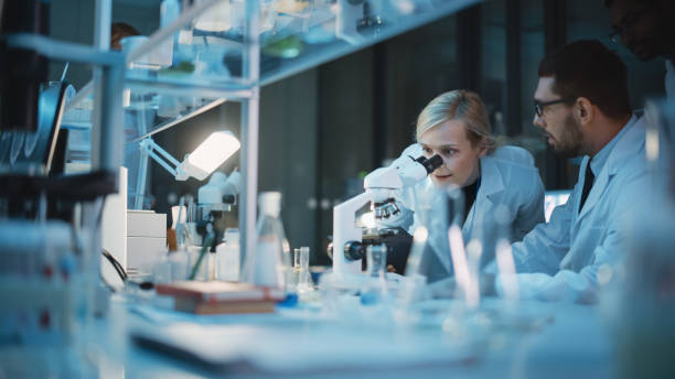 medical development laboratory: team of female and male scientist using microscope, analyzes petri dish sample. specialists working on medicine, biotechnology research in advanced pharma lab - science life medical research healthcare and medicine imagens e fotografias de stock