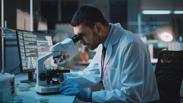 istock Medical Research Scientist Conducts DNA Experiments Under Digital Microscope in a Biological Applied Science Laboratory. Handsome Caucasian Lab Engineer in White Coat Working on Vaccine and Medicine. 1309776271