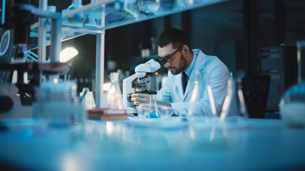 istock Medical Development Laboratory: Caucasian Female Scientist Looking Under Microscope, Analyzes Petri Dish Sample. Specialists Working on Medicine, Biotechnology Research in Advanced Pharma Lab 1309776274