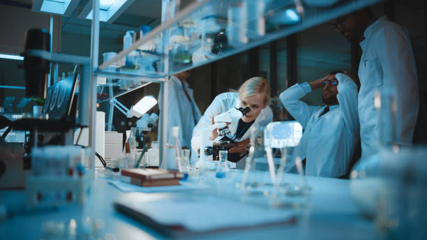 istock Happy Male Reseach Scientist Makes an Important Discovery While Researching Samples Under the Microscope. Happy Colleagues Congratulate it and Share Success with Fellow Bioengineers. 1309776279