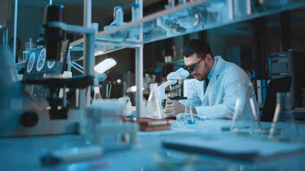istock Medical Development Laboratory: Caucasian Female Scientist Looking Under Microscope, Analyzes Petri Dish Sample. Specialists Working on Medicine, Biotechnology Research in Advanced Laboratory 1309776280
