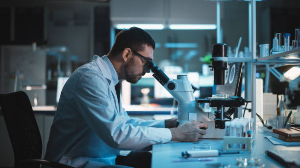 istock Medical Development Laboratory: Caucasian Female Scientist Looking Under Microscope, Analyzes Petri Dish Sample. Specialists Working on Medicine, Biotechnology Research in Advanced Laboratory 1309776299