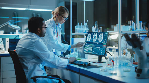istock Female Research Scientist Has a Conversation with Bioengineer About the Effects of Different Pharmaceutical Drugs on Brain. They Look at Computer Software Visualization in a Modern Science Laboratory. 1309776396