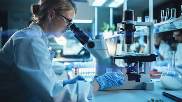 istock Medical Research Scientist Looks at Biological Samples Under Digital Microscope in Applied Science Laboratory. Beautiful Caucasian Lab Engineer in White Coat Working on Vaccine and Medicine. 1309776403