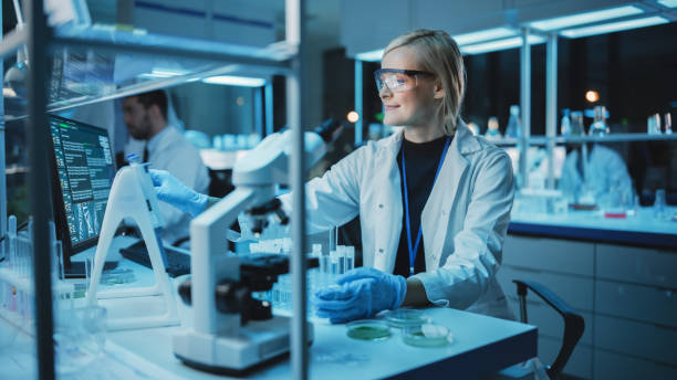 Female Research Scientist Uses Micropipette to Mix Liquids in a Sample Test Tube in a Modern Laboratory. Scientists are Conducting DNA Research with the Help of Technology, Microscopes and Computers. una científica de investigación utiliza micropipette para mezclar líquidos en un tubo de ensayo de muestra en un laboratorio moderno. los científicos están llevando a cabo investigaciones de adn con la ayuda de tecnología, microscopios y computadoras