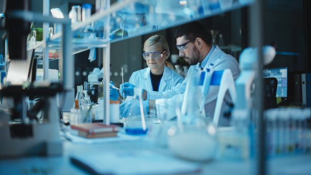 istock Female and Male Medical Research Scientists Have a Conversation While Conducting Experiments in Test Tubes with Liquid Samples with and in Beakers with Solid Speciments. Modern Science Laboratory. 1309776457