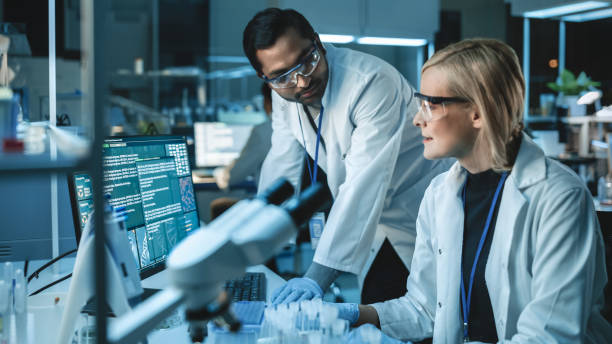 istock Female Research Scientist Has a Conversation with Bioengineer About the Latest DNA Experiments in a Modern Laboratory. She is Doing Important Medical Research with Help of Modern Computer Software. 1309776459