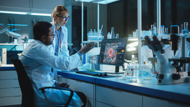 istock Female Research Scientist with Bioengineer Working on a Personal Computer with Screen Showing Virus Analysis Software User Interface. Scientists Developing Vaccine, Drugs and Antibiotics in Laboratory 1309776483