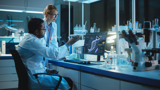 istock Female Research Scientist with Bioengineer Working on a Personal Computer with Screen Showing DNA Analysis Software User Interface. Scientists Developing Vaccine, Drugs and Antibiotics in Laboratory 1309776492