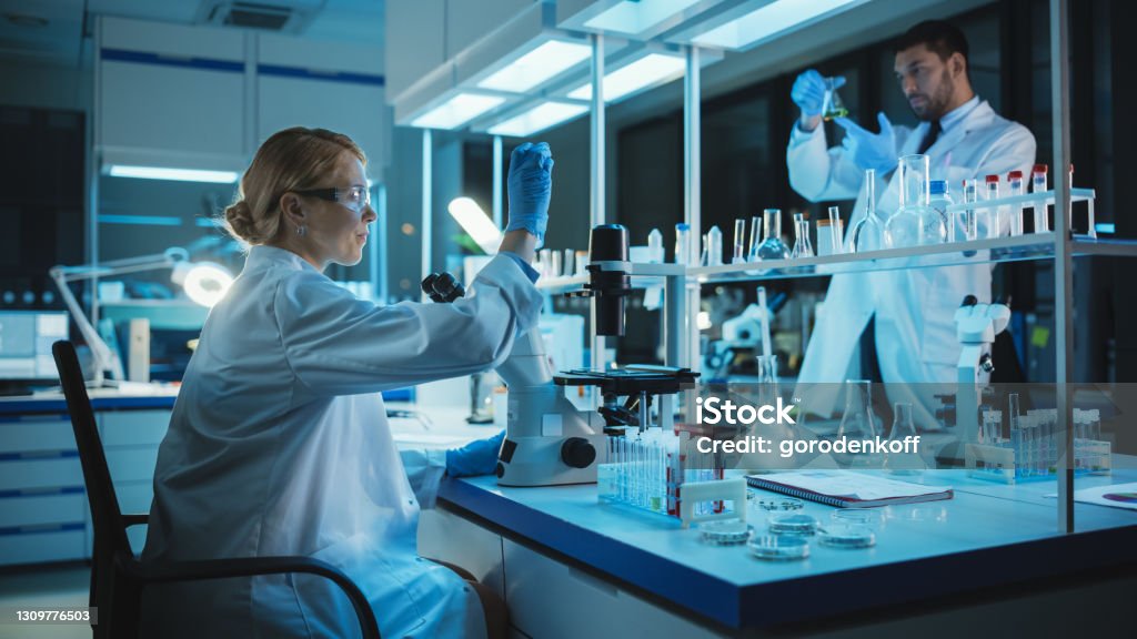 Female Medical Research Scientist Looks at Biological Samples Before Analysing it Under Digital Microscope in Applied Science Laboratory. Lab Engineer in White Coat Working on Vaccine and Medicine. Science Stock Photo