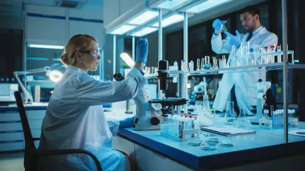 Photo of Female Medical Research Scientist Looks at Biological Samples Before Analysing it Under Digital Microscope in Applied Science Laboratory. Lab Engineer in White Coat Working on Vaccine and Medicine.