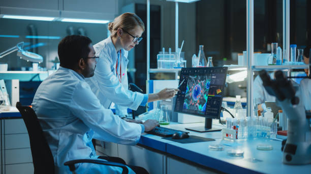 istock Female Research Scientist with Bioengineer Working on a Personal Computer with Screen Showing Virus Analysis Software User Interface. Scientists Developing Vaccine, Drugs and Antibiotics in Laboratory 1309776504