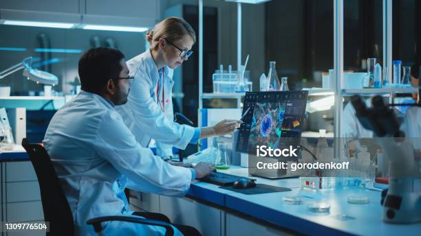 Female Research Scientist With Bioengineer Working On A Personal Computer With Screen Showing Virus Analysis Software User Interface Scientists Developing Vaccine Drugs And Antibiotics In Laboratory Stock Photo - Download Image Now