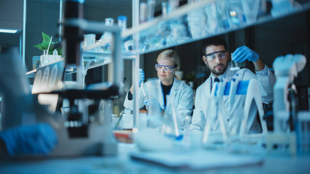 istock Female and Male Medical Research Scientists Have a Conversation While Conducting Experiments in Test Tubes with Liquid Samples with and in Beakers with Solid Speciments. Modern Science Laboratory. 1309776505