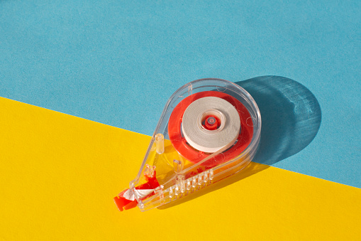 Office red tool tape corrector isolated on a yellow and blue background