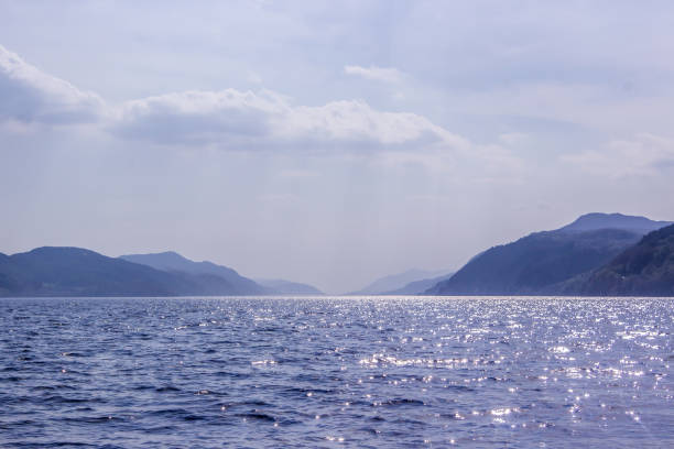 Lochness in shades of Blue Looking south over Loch ness, Scotland, towards the mountains forming the edges of the Great Glen, with sunlight reflecting of small waves, This loch, famous for its mythical monster, is situated in an old Glacial valley which followed the Great Glen Fault line. With a depth of 240m and a length of almost 36km it is the largest lake by water volume and second largest by surface are in the British Isles drumnadrochit stock pictures, royalty-free photos & images