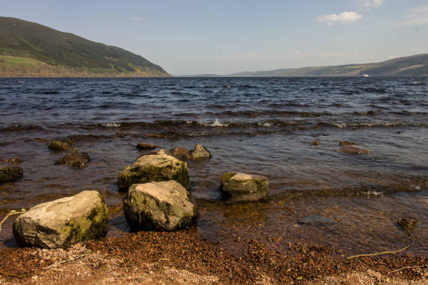 On the Shore of Loch Ness Large Boulders at the water"u2019s edge of Loch Ness Scotland, on a clear windy day. This loch, famous for its mythical monster, is situated in an old Glacial valley which followed the Great Glen Fault line. With a depth of 240m and a length of almost 36km it is the largest lake by water volume and second largest by surface are in the British Isles drumnadrochit stock pictures, royalty-free photos & images
