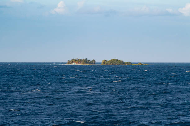 istock Two distant tree covered islands with blue ocean in the foreground and blue and grey sky background 1309777359