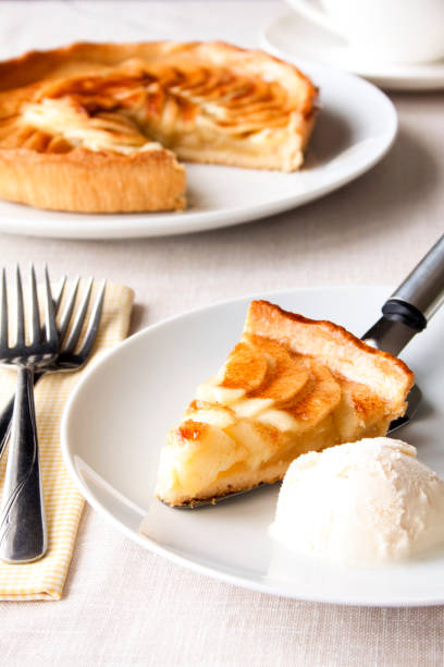 Apple Pie A slice of apple pie served with vanilla ice cream
Served on a white table with a yellow checked napkin, with the pie in the background. apple pie and ice cream stock pictures, royalty-free photos & images
