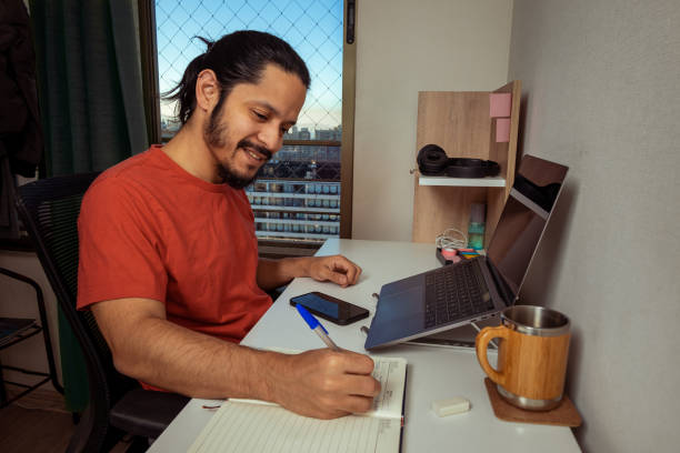 Young man with smily face doing homework and studying at home. Man working at home.