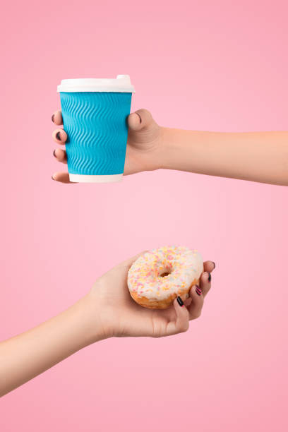 istock Womans hands holding colorful donut and coffee cup over pink background. 1309778860