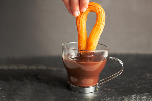 Hand dunking churro into hot chocolate in a glass cup