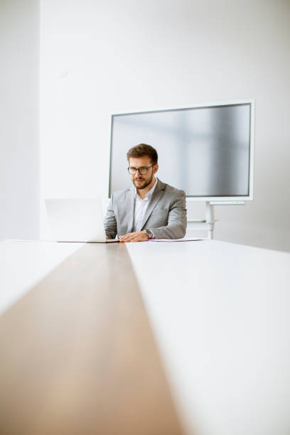 istock Young man working on laptop in bright office with big screen behind him 1309779891