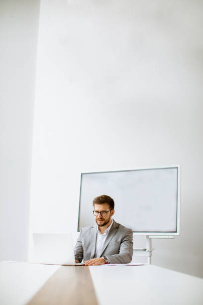 istock Young man working on laptop in bright office with big screen behind him 1309779893