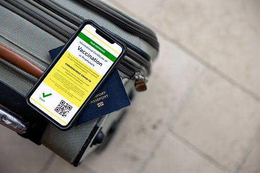 Digital vaccine passport app in mobile phone for travel during Covid-19 pandemic. The mobile phone and passport are on a suitcase.