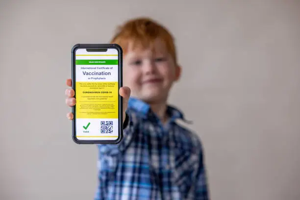 Photo of Vaccinated boy using digital vaccine passport app in mobile phone at customs for travel during Covid-19 pandemic