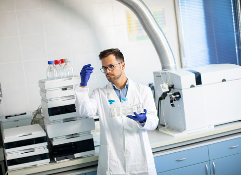 Handsome young researcher workin with chemical samples in laboratory with HPLC system and  chromatography equipment